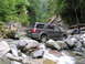2000 Jeep Cherokee - SUV driving through a rocky stream in a wooded area.