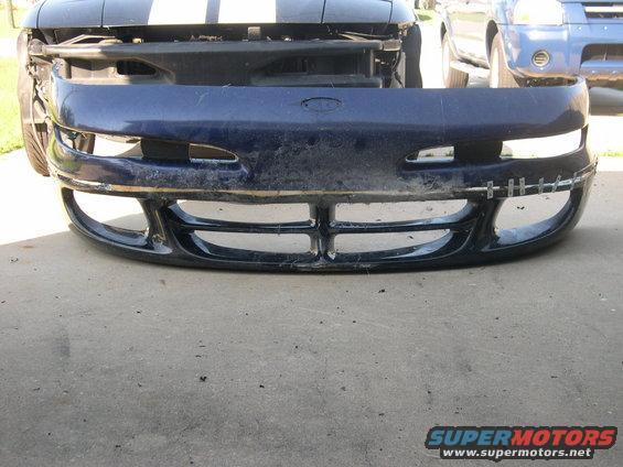 Blue bumper with racing stripes visible on hood. Another vehicle is parked behind