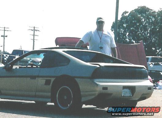 Silver 1984 Pontiac Fiero with black rear decklid and a man standing behind it
