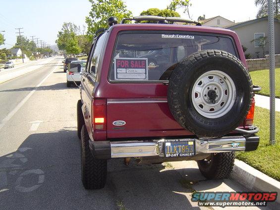 Red Ford Bronco II parked on street, spare tire on rear door. 'For Sale' sign in window. License plate reads 1LKT853