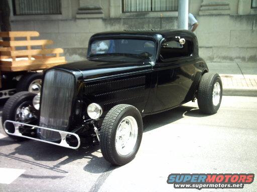 Black 1934 Ford hot rod coupe with chrome grille and wide rear tires
