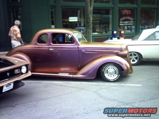 Purple and gold custom coupe hot rod, side view, with a white car behind it