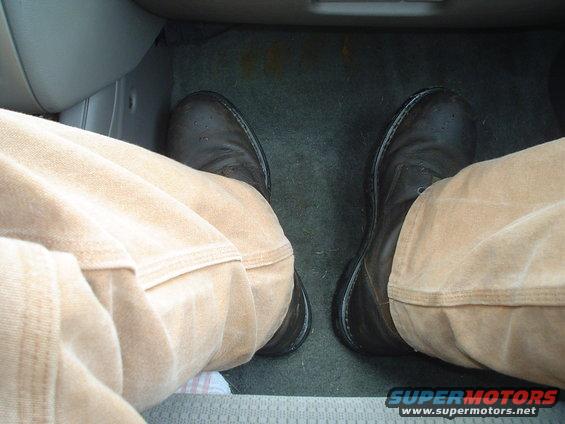 Driver's feet in brown boots and tan pants, visible on the floor mat inside a vehicle