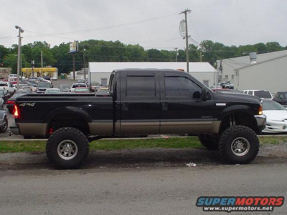 Lifted black pickup truck with tan lower body, 4x4 badging on the bed, parked on a street