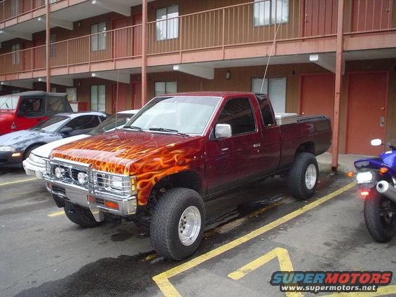 Maroon pickup truck with flame decals parked in a lot, other vehicles visible