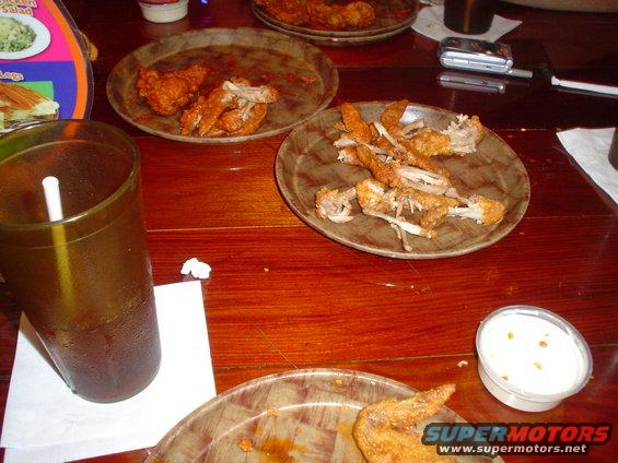 table with plates of leftover fried chicken, a drink, and a small cup of dip
