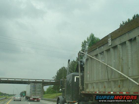 dump truck driving on highway, other trucks and cars visible, overcast sky