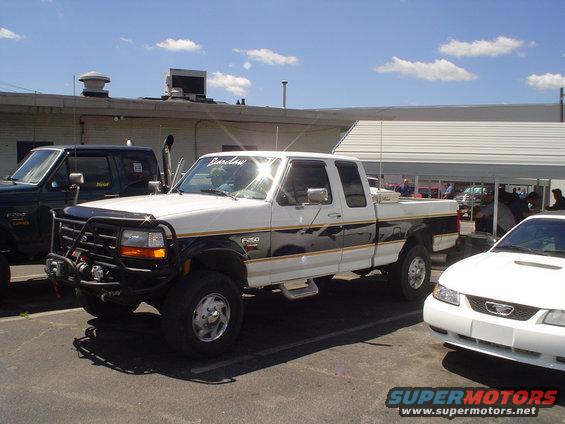White Ford F-250 truck with black and gold stripes, bull bar, and dual exhaust pipes