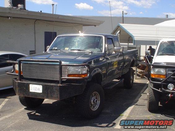 Dark green pickup truck, 3/4 front view, with aftermarket bumper and grille. License plate reads UIEZLOC