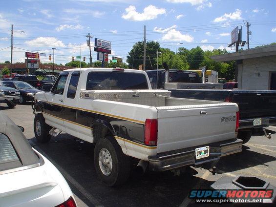White Ford pickup truck with a toolbox in the bed, parked next to other vehicles