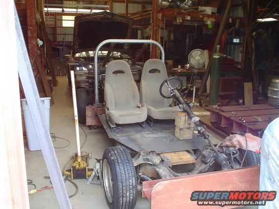 vehicle chassis with two seats, roll cage, and steering column, in a workshop