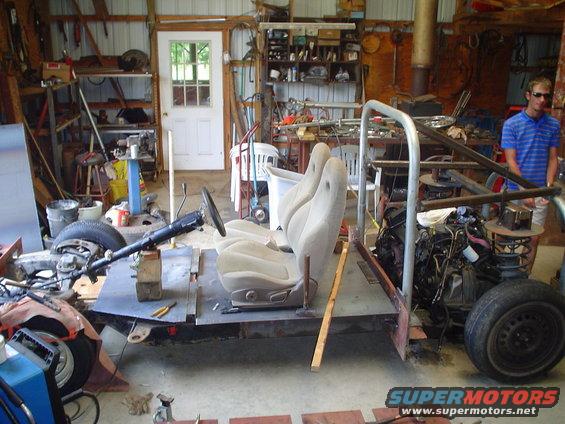 Vehicle chassis with two bucket seats, steering column, and engine in a workshop