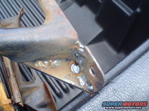 Welded metal bracket with rust and rough welds, resting on a textured surface