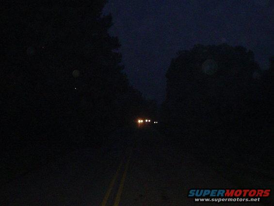 Two vehicles with headlights on driving on a dark road at night