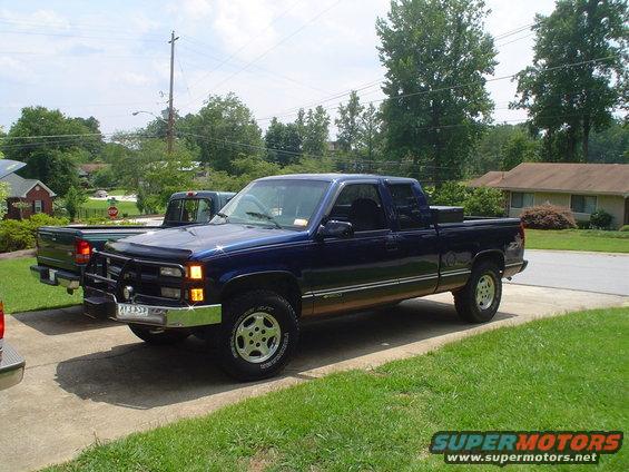 Dark blue pickup truck parked on driveway, another truck behind it. Toolbox in bed