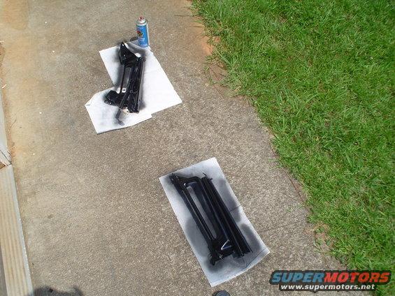 Two black painted metal parts on paper towels on concrete, with a spray can