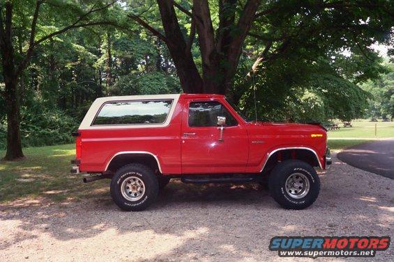 Red Ford Bronco parked under a tree. It has a white removable top and off-road tires
