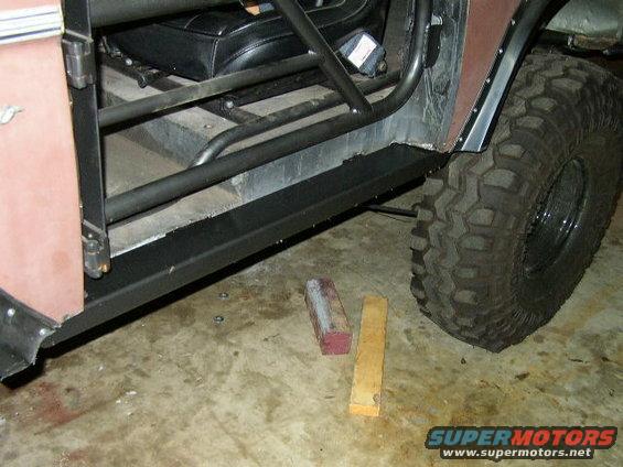 1995 Ford Bronco interior with roll cage and aftermarket sliders, showing a brown door and large off-road tire