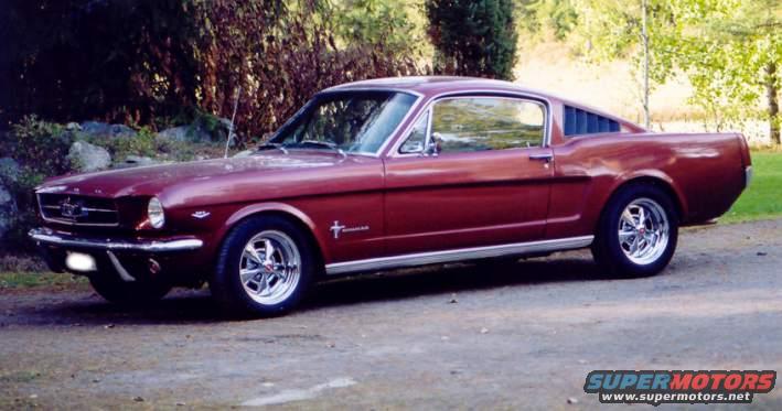 Maroon 1965 Ford Mustang Fastback parked on a dirt road, chrome wheels, side view