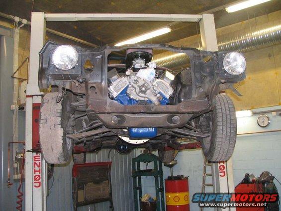 car body on lift, front end removed, showing engine and suspension components