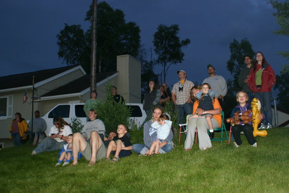 People sitting on a grassy lawn at dusk, watching an unseen event