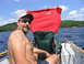 1986 Ford Bronco - A man smiles while holding a red shirt in a boat on a sunny day with a lake and trees in the background.