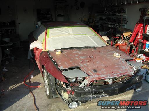 Red car with hood and front end disassembled, masked for painting. Headlights are visible