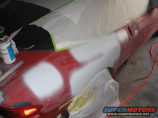 Car fender being prepped with body filler and primer for repair. Spray can and masking paper visible
