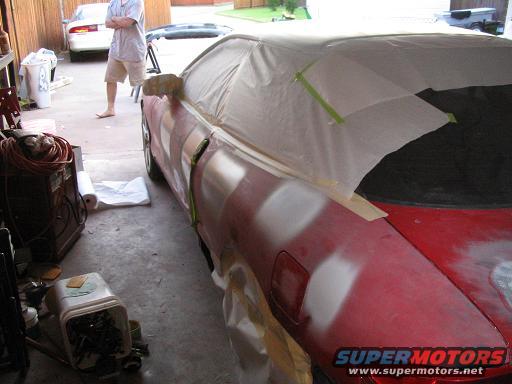 Red car with masking tape and primer patches, parked next to a white car
