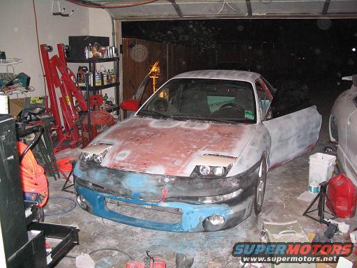 Car in garage, looks like it's being prepped for paint. Has pop-up headlights and a blue bumper