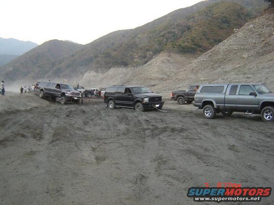 Several SUVs and trucks stuck in sand, one being towed by another