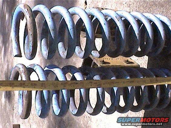 Two large suspension coil springs, one above the other, with a yellow strap across the lower one