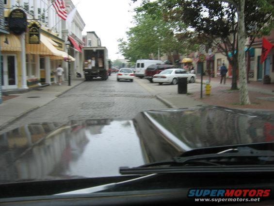 Car hood reflecting a street scene with shops and other vehicles
