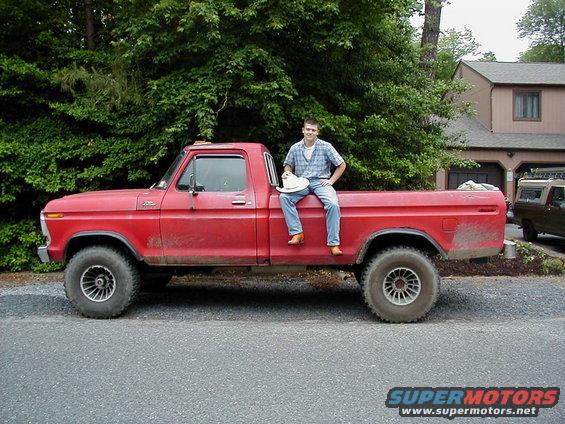 guy sitting on side of red pickup truck, another truck parked in driveway behind