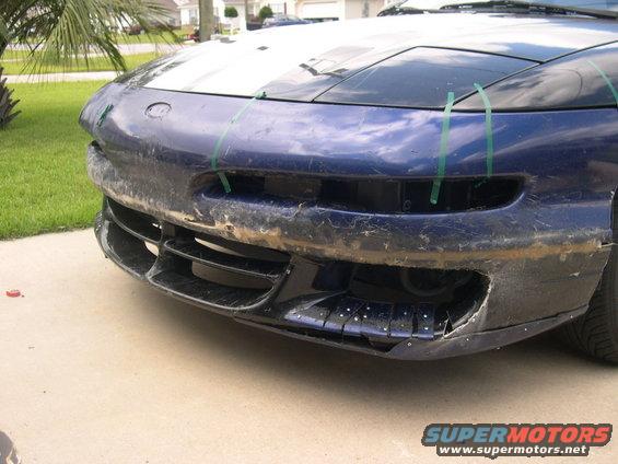 Front bumper of a blue car, looks like it needs repair. Green tape is holding parts of it together