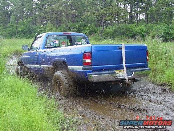 Blue pickup truck stuck in mud, rear view, lifted suspension, off-road tires, license plate EN-893K