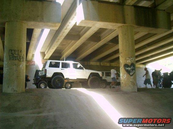 White Jeep Cherokee parked under a bridge, with another vehicle behind it