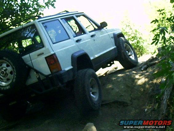 White Jeep Cherokee XJ climbing over logs on a dirt trail