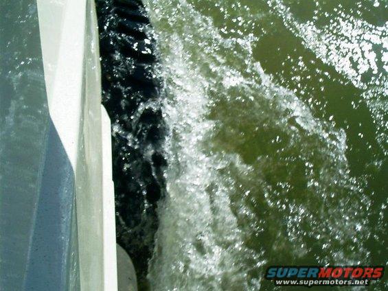 Side of a boat cutting through green water, creating a wake