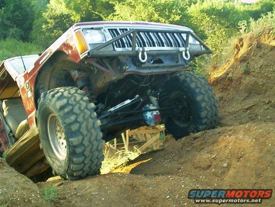 Modified Jeep Cherokee with large tires climbing a dirt hill, custom front bumper and grille visible
