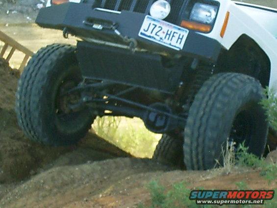 White Jeep Cherokee with aftermarket bumper and large tires on dirt terrain