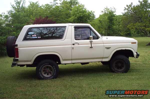 White Ford Bronco parked on grass with trees in background. Spare tire mounted on rear