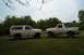 1985 Ford Bronco - Two white Ford Broncos, an SUV and a pickup truck, are parked side-by-side on a grassy field under a cloudy sky.