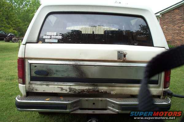 Rear of a white Ford Bronco, showing the tailgate, bumper, and a towing hitch. Some rust is visible on the lower tailgate