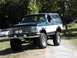 1994 Ford Bronco - Modified 1994 Ford Bronco with lifted suspension and large tires parked outdoors. Another car is visible in the background.