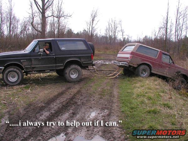 Side view of a black 1987 Ford Bronco towing a maroon Bronco out of a muddy ditch