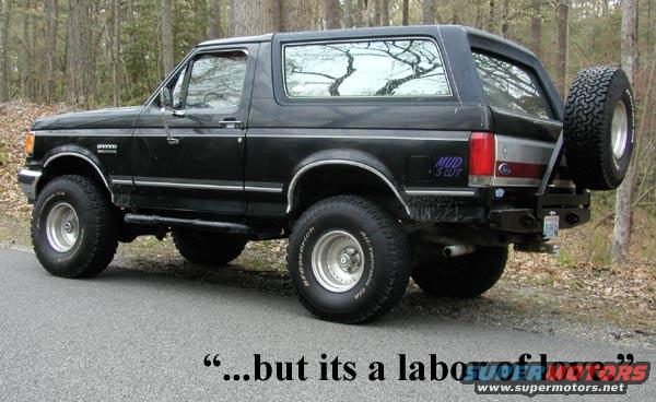 Black Ford Bronco parked on a road, side view. Has a spare tire on the back