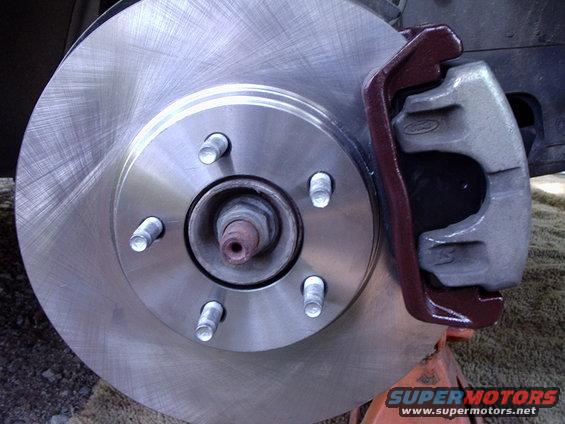 Car brake rotor with a red-painted caliper, supported by an orange jack stand