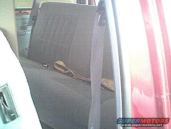 Vehicle interior showing gray fabric rear seat and seatbelt, with red exterior visible through the window