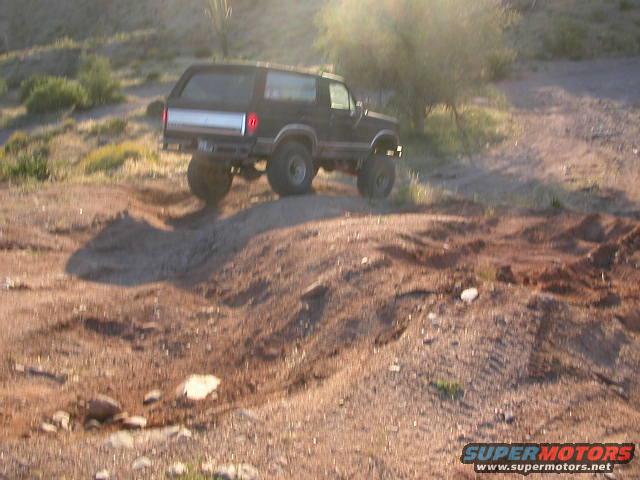 Black Ford Bronco climbing a dirt hill off-road. Lifted suspension and large tires visible